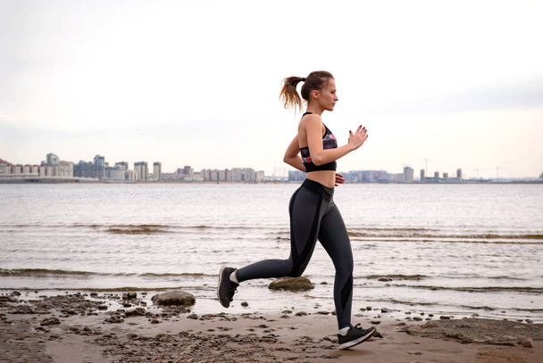  slim athletic European girl in sportswear runs along the beach  - Foto, afbeelding