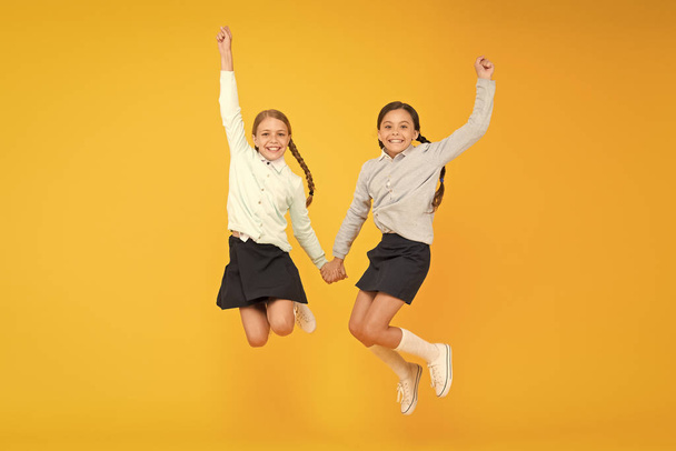 Cuties in mid air. Active children jumping high on yellow background. Happy girls enjoying active lifestyle. School friends having fun activities together. Active generation. Active and energetic - Фото, изображение