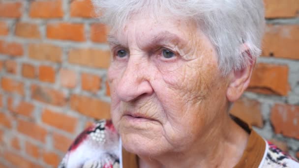 Grootmoeder zit buiten met iemand te praten. Portret van een oudere vrouw met een ernstige gezichtsuitdrukking. Oma communiceert met iemand. Langzame beweging Close-up - Video