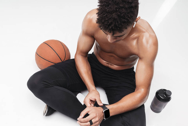 Photo of shirtless african american man using smartwatch while sitting - 写真・画像