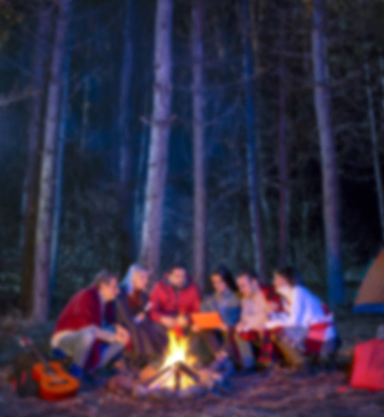 Homályos színes elvont konceptuális jelenet turistákkal tábortűz körül ülnek kempingsátor közelében az erdőben éjszaka. Egy csapat diák a szabadtéri tűznél. Utazási tevékenység és nyaralás hétvége koncepció - Fotó, kép
