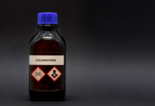 Chloroform in brown laboratory bottle stock images. A bottle of chloroform with inscription. Brown lab bottle. Brown glass container. Phial with warning pictograms on a black background - 写真・画像