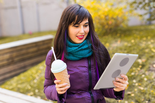 Technológiák, városi és ember koncepció - Egy diák fiatal nő könyvet vagy táblagépet olvas egy városi őszi parkban - Fotó, kép