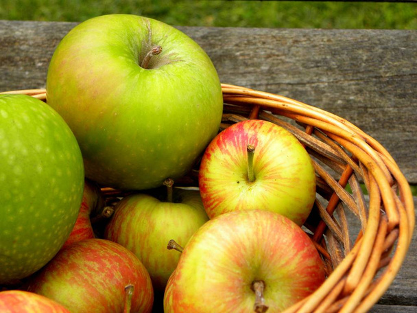green and red apples in wicker basket on wooden background - Fotoğraf, Görsel