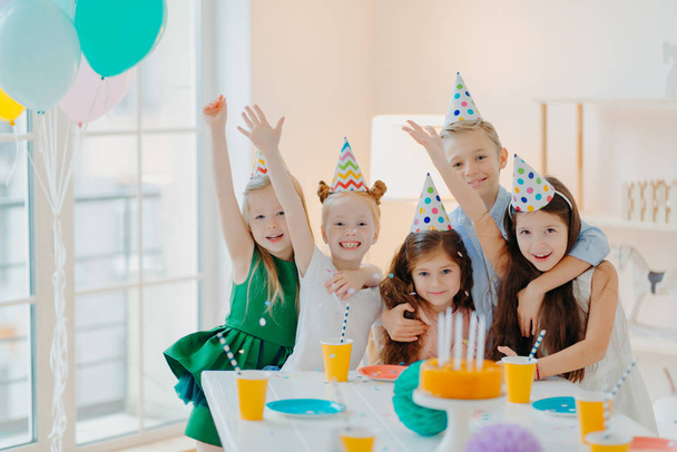 Kids party and celebration concept. Group of small children friends make photo together, raise arms and smile gladfully, have birthday party, festive event, foolish around - Photo, Image