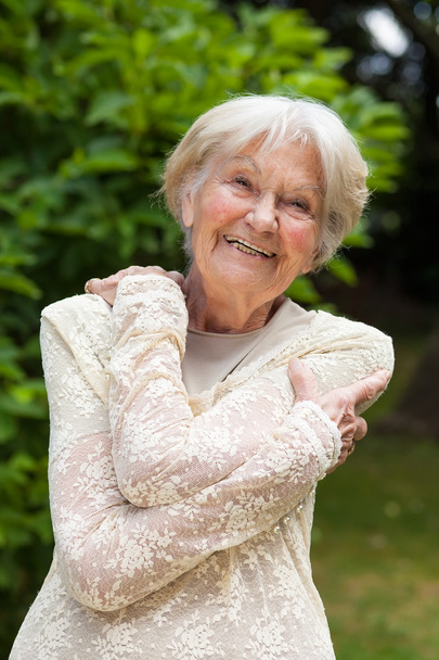 Пожилая женщина обнимает себя руками в саду
 - Фото, изображение