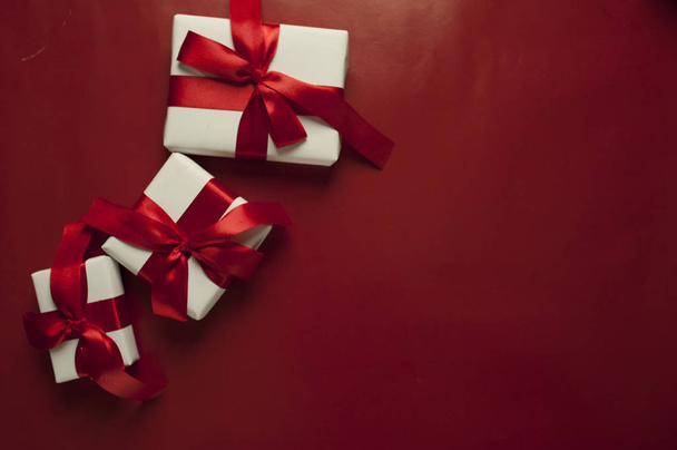 Karácsonyi üdvözlőlap ajándékdobozokkal piros háttérrel. Fehér karácsonyi ajándékdobozok piros háttérrel. Top view helyet a gratulációk - Fotó, kép