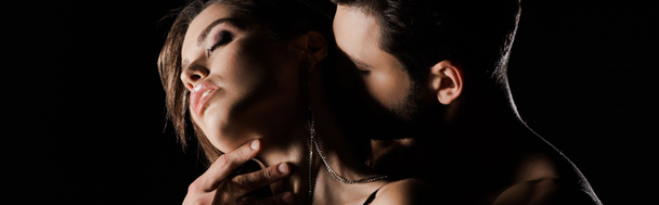 панорамный снимок мужчины целующего соблазнительную женщину с закрытыми глазами, изолированными на черном
  - Фото, изображение