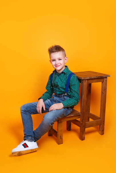 Fashionable kid model in trendy clothes sitting on yellow background - Valokuva, kuva