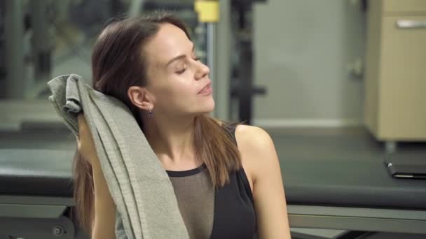 Young attractive woman resting and wiping sweat from her face with a towel after an active workout in the gym. - Filmagem, Vídeo