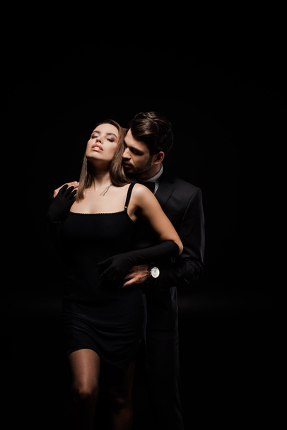 handsome man in suit hugging attractive woman isolated on black  - Fotografie, Obrázek