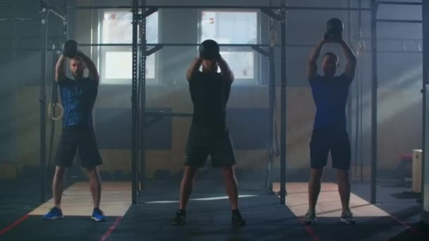 スローモーション: 3人の友人フィットネスアスリート男性は、ジムで一緒に重量挙げを楽しむ強力な強さの運動友達を行うケトルベルの重みを使用して筋肉ボディビルダーを訓練します. - 映像、動画