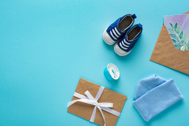 Top view of baby booties, pacifier and envelopes with greeting card on blue background, concept of mothers day  - Foto, afbeelding