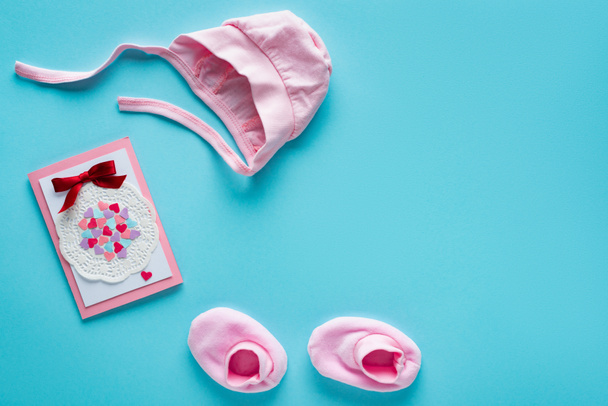 Top view of pink baby clothes and greeting card on blue background, concept of mothers day  - Photo, Image