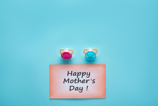 Vista superior de la tarjeta de felicitación con letras feliz día de las madres y chupetes sobre fondo azul
 - Foto, Imagen