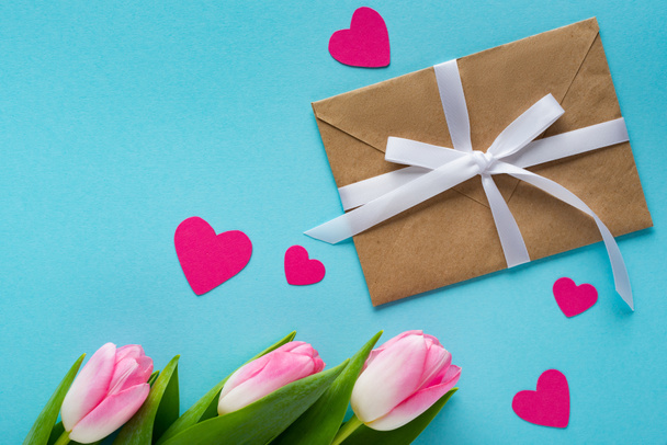 Верхний вид конверта, бумажных сердец и тюльпанов на голубом фоне
 - Фото, изображение