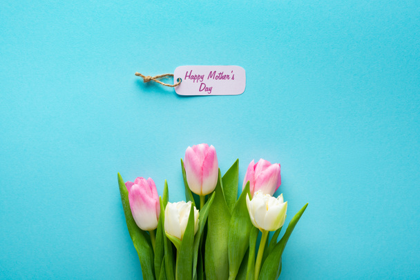 Top view of paper label with happy mothers day lettering and tulips on blue background - Photo, Image