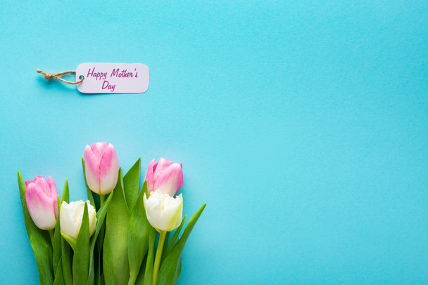 Widok góry etykiety papierowej z szczęśliwy dzień matki liternictwo i tulipany na niebieskiej powierzchni z miejsca kopiowania - Zdjęcie, obraz
