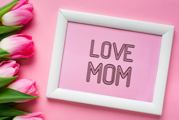 Top view of love mom lettering in frame near tulips on pink background - Фото, зображення