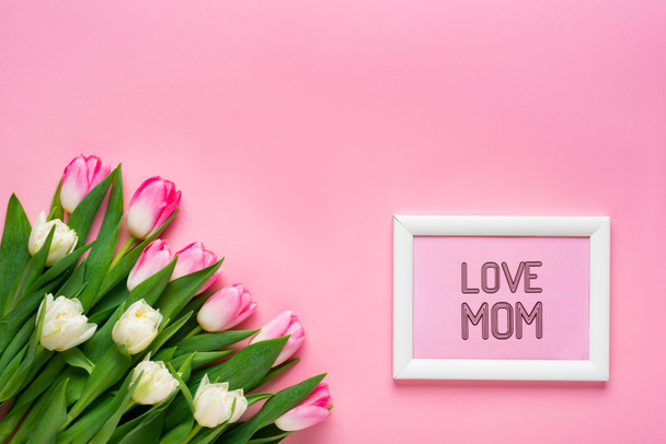 Top view of tulips and frame with love mom lettering on pink surface - Fotoğraf, Görsel