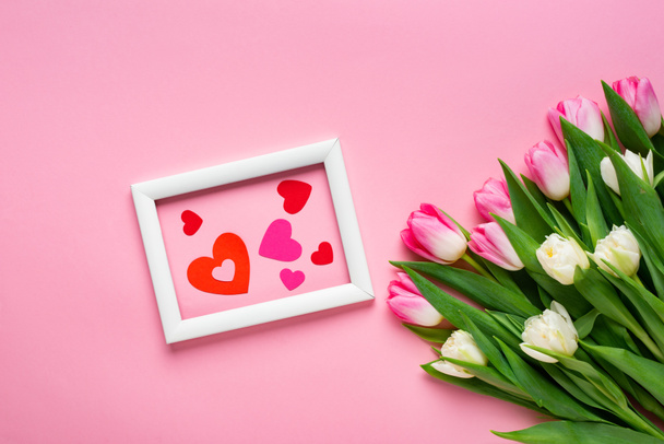 Vista superior de corazones de papel en marco cerca de ramo de tulipanes sobre fondo rosa
 - Foto, imagen