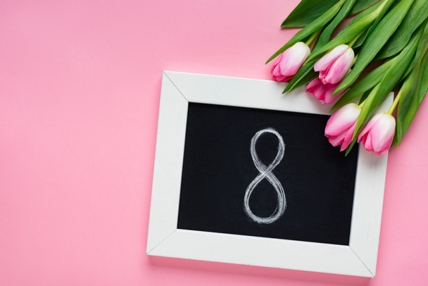 Vista superior de pizarra con 8 números cerca de tulipanes sobre fondo rosa
 - Foto, imagen