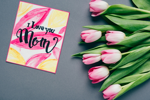Bovenaanzicht van boeket van tulpen en wenskaart met ik hou van je moeder belettering op grijze achtergrond - Foto, afbeelding