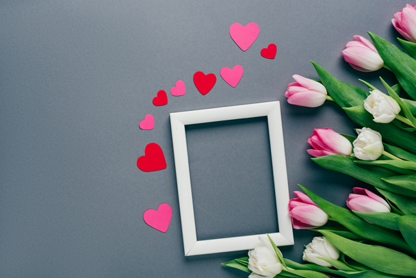 Top view of white frame with paper hearts and tulips on grey surface - Photo, Image