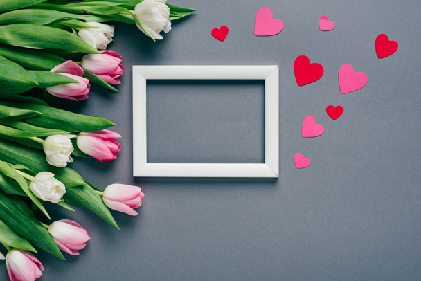 Top view of white empty frame with paper hearts and tulips on grey background - Foto, imagen