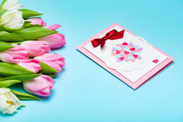 Букет тюльпанов рядом с открыткой на голубой поверхности
 - Фото, изображение