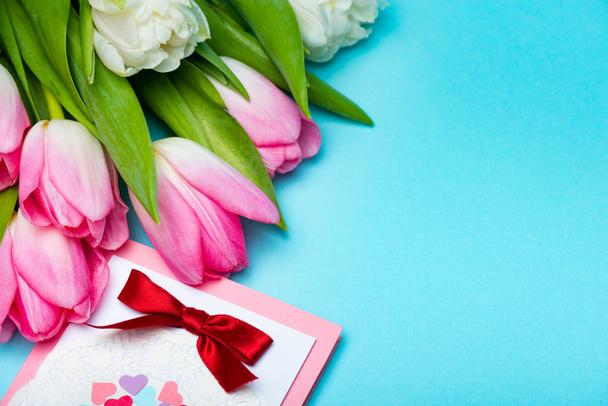 Close up view of bouquet of tulips near greeting card on blue surface - Foto, Bild