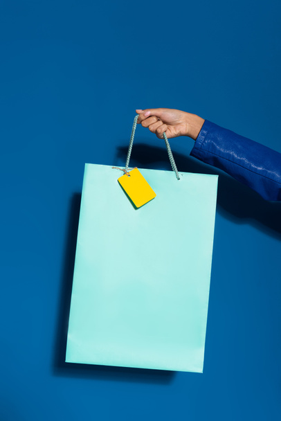 vista recortada de mujer afroamericana sosteniendo bolsa de compras con etiqueta en blanco en azul
 - Foto, imagen