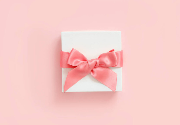 Valkoinen lahjapakkaus, jossa rusetti vaaleanpunaisella taustalla
 - Valokuva, kuva