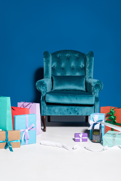 shopping bags and gift boxes near payment terminal with check on blue background with velour armchair - Фото, изображение