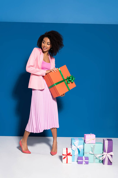 elegant smiling african american woman near gifts on blue background - Photo, Image