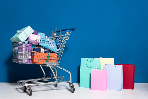 shopping bags, trolley with gifts on blue background - Foto, Imagen