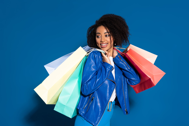 smiling african american woman with shopping bags on blue background - Fotografie, Obrázek