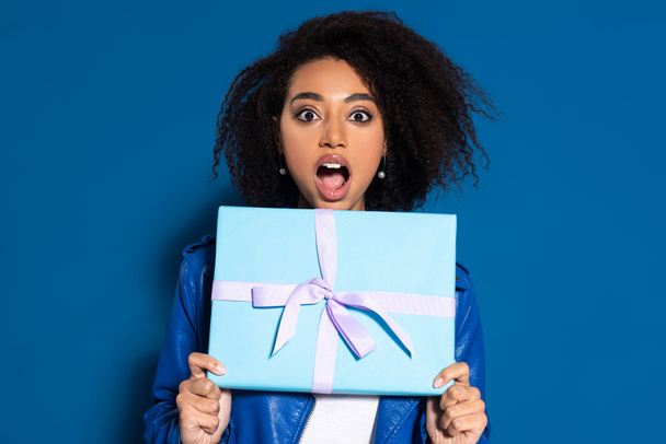 shocked african american woman holding present on blue background - Foto, imagen