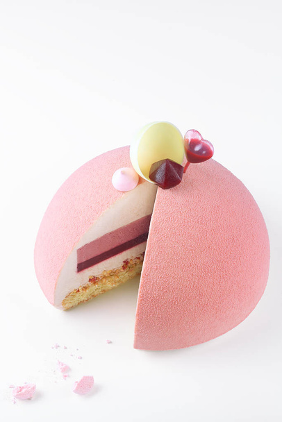 Contemporary Ruby Chocolate Dome Mousse Cake, covered with ruby velvet spray, decorated with meringue cookies, raspberry jelly, white chocolate shell and heart shape sauce capsule, on white background. - Photo, Image