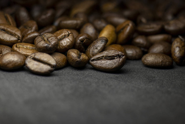 Koffie in bonen op donkere achtergrond. Abstracte achtergrond textuur.Koffiebonen textuur. Voedselachtergrond van koffiebonen - Foto, afbeelding