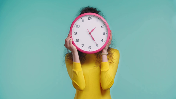 serious woman obscuring face with clock isolated on turquoise - Footage, Video