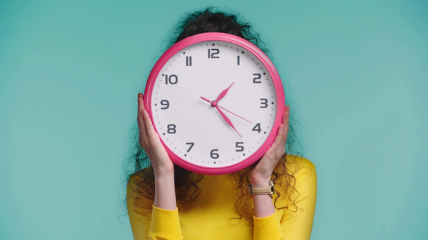 smiling woman obscuring face with clock isolated on turquoise  - Footage, Video