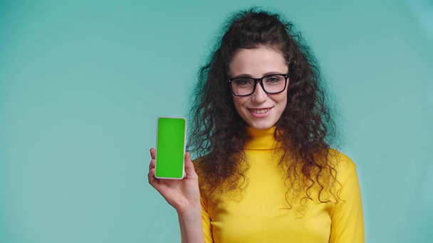 smiling woman showing smartphone isolated on turquoise  - Video, Çekim