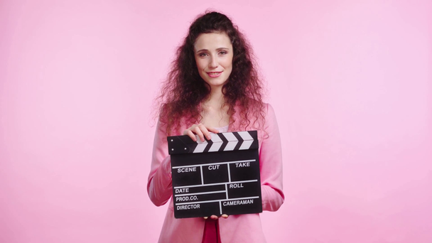 glimlachende vrouw klappen met clapboard geïsoleerd op roze - Video