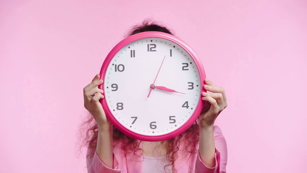 serious woman obscuring face with clock isolated on pink - Footage, Video