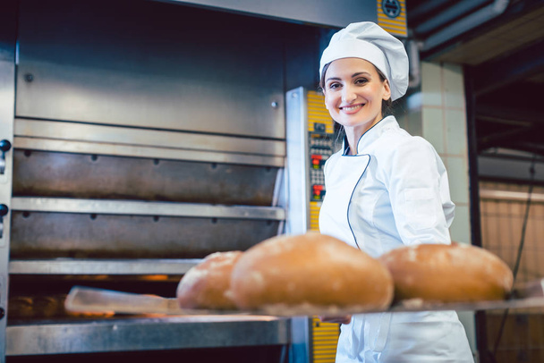 Leipurinainen esittelee tuoretta leipää lapiolla
 - Valokuva, kuva