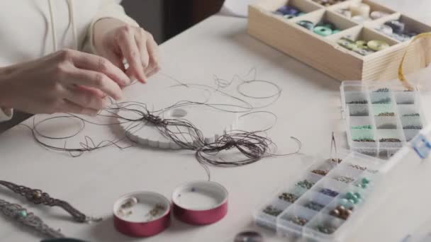 Lifestyle concept, werken vanuit huis om je leven opnieuw uit te vinden: close-up van de vrouw handen maken macrame geknoopte sieraden met stenen kralen en gereedschappen op lichte houten tafel - Video