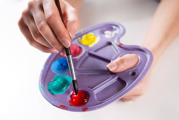 Festőecset női művész kezét keverés festékek egy palettán. Lány kezében műanyag paletta különböző színekkel és keverés. Művészet és festészet. Közelkép, szelektív fókusz - Fotó, kép