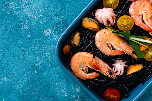 vista superior macarrão preto com frutos do mar-camarão, mexilhões, polvo, tomates cereja em placa azul sobre fundo cinza, conceito de cozinha mediterrânica
 - Foto, Imagem