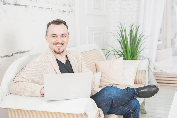 Beau homme heureux travaillant à l'aide d'un ordinateur portable sur le canapé à la maison
 - Photo, image